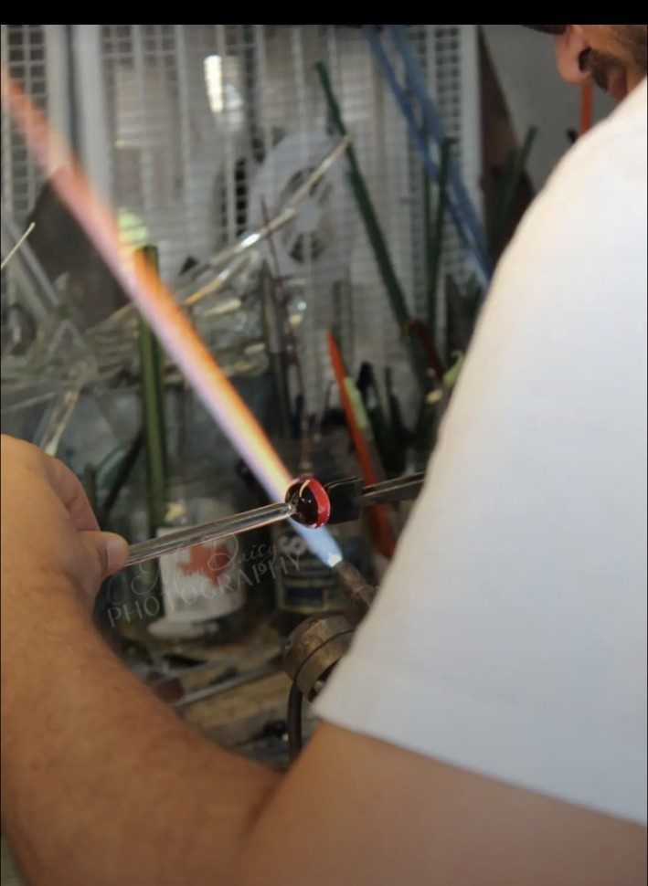 Close view of Jose Valdes working a red glass piece